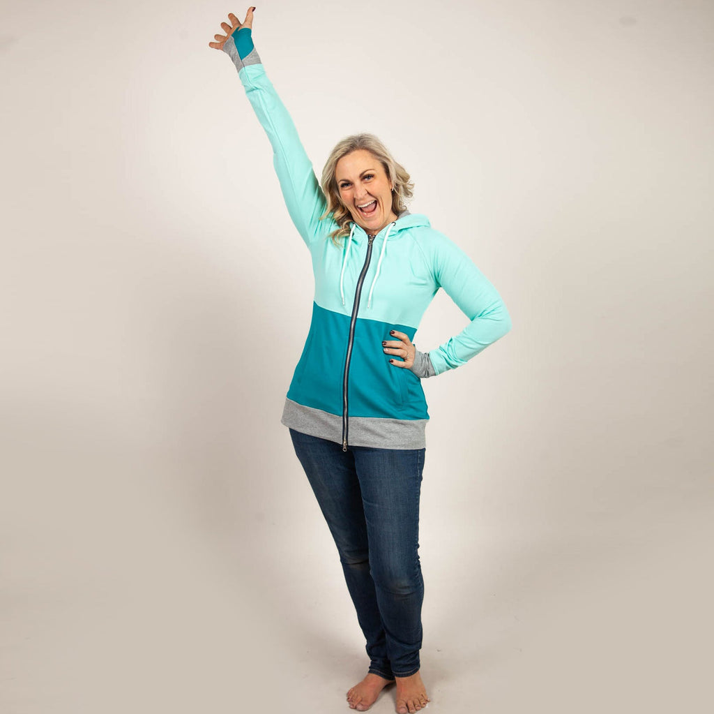A woman wearing a color-block hoodie with mint green at the top, dark turquoise at the bottom, and heather gray accents. The hoodie has a full double zip, hood, thumbholes, and side pockets. shown in size medium