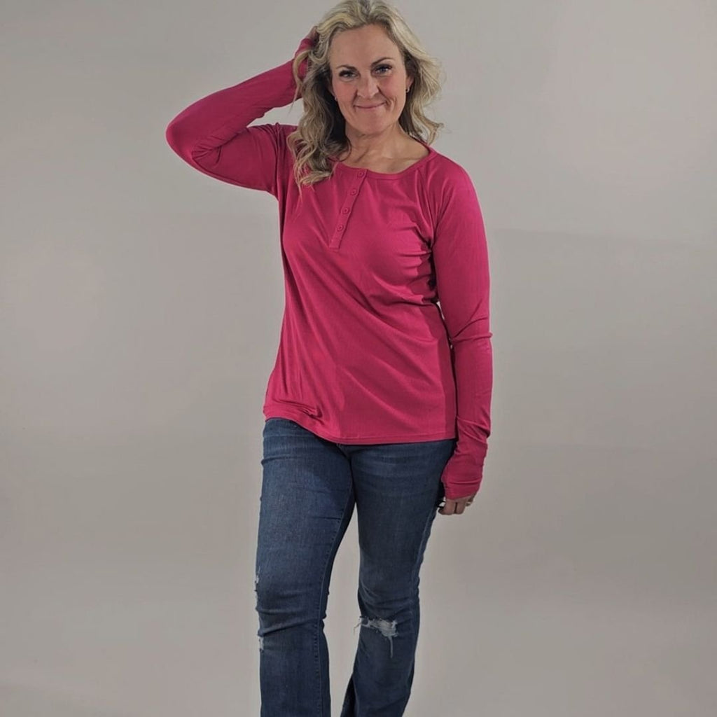 A woman wearing a raspberry red long sleeve, semi-fitted, henley top with thumbholes. shown in size medium