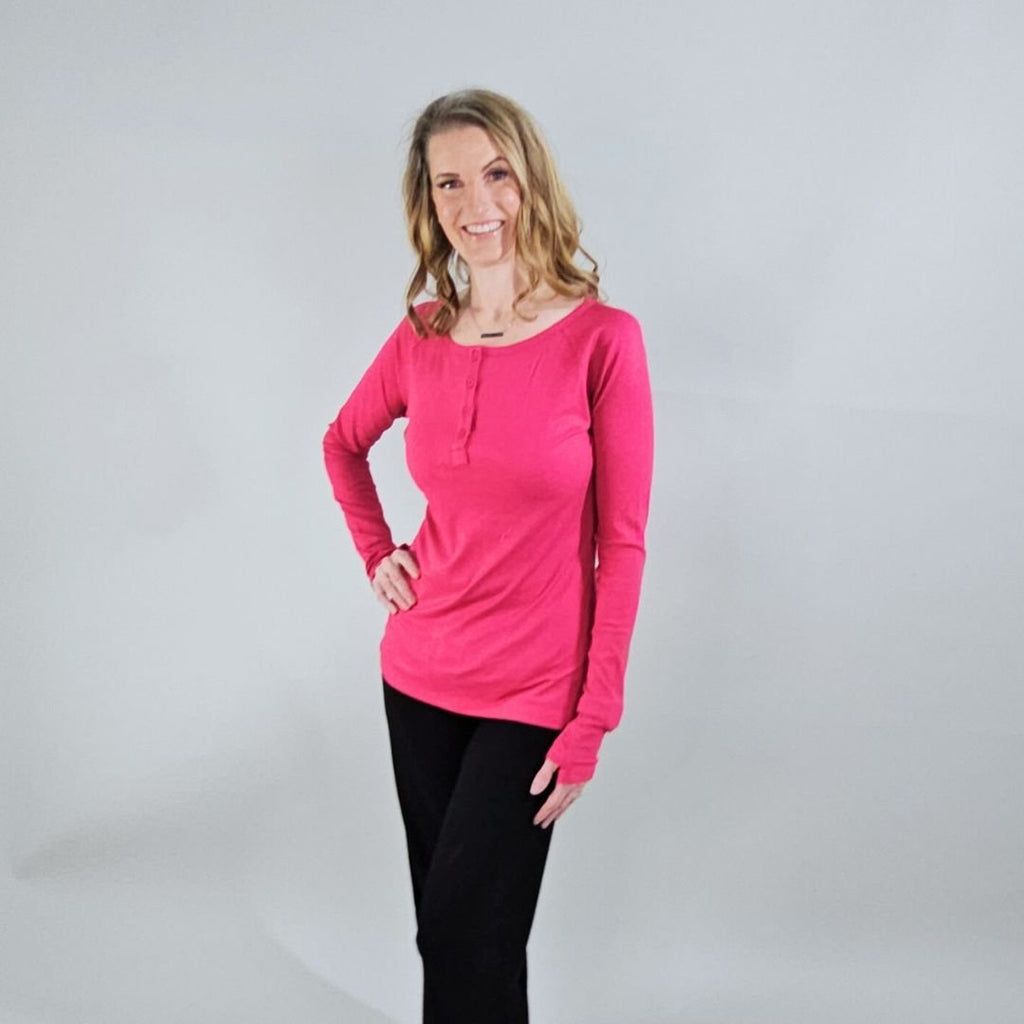 A woman wearing a raspberry red long sleeve, semi-fitted, henley top with thumbholes. shown in size XS