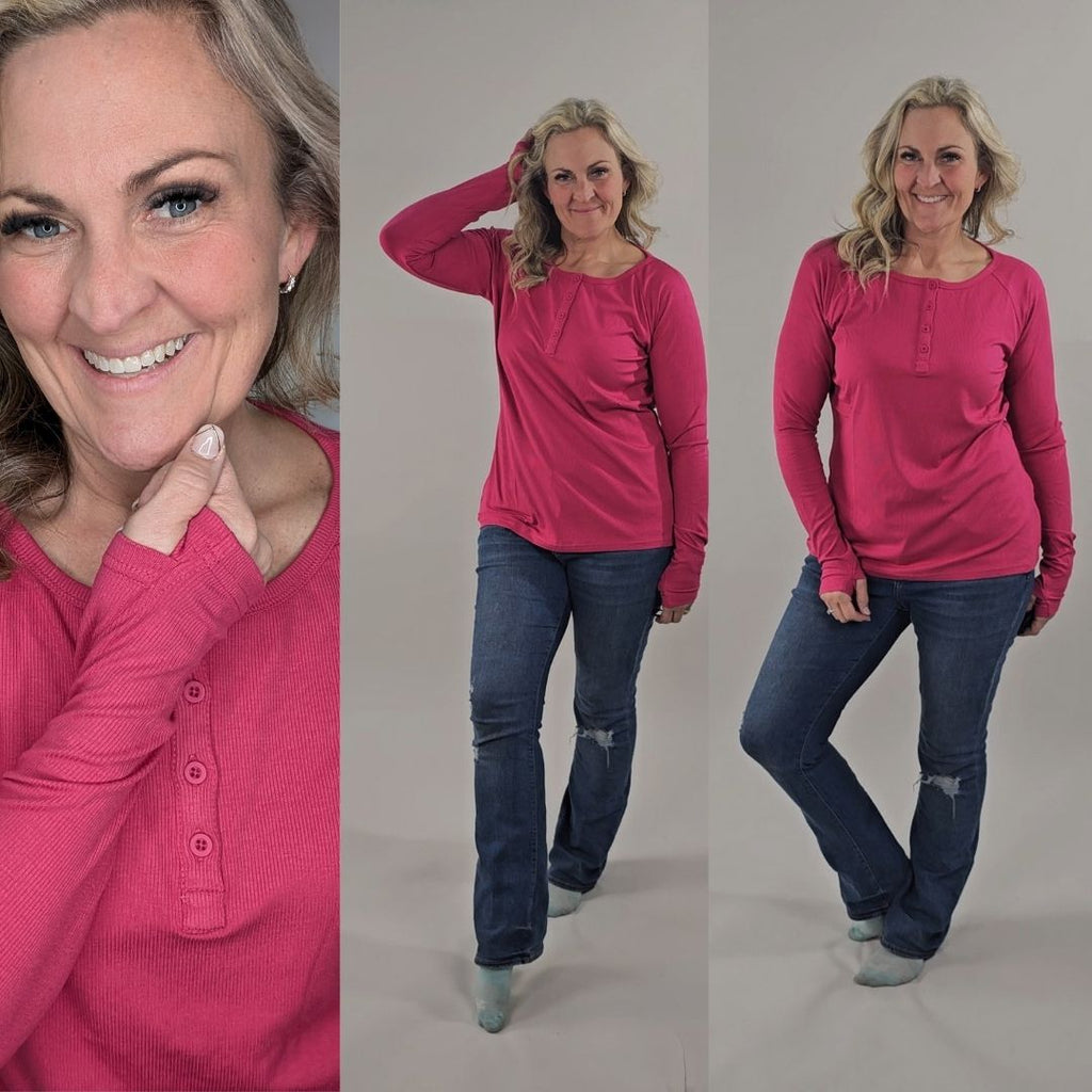 A woman wearing a raspberry red long sleeve, semi-fitted, henley top with thumbholes. shown in size medium