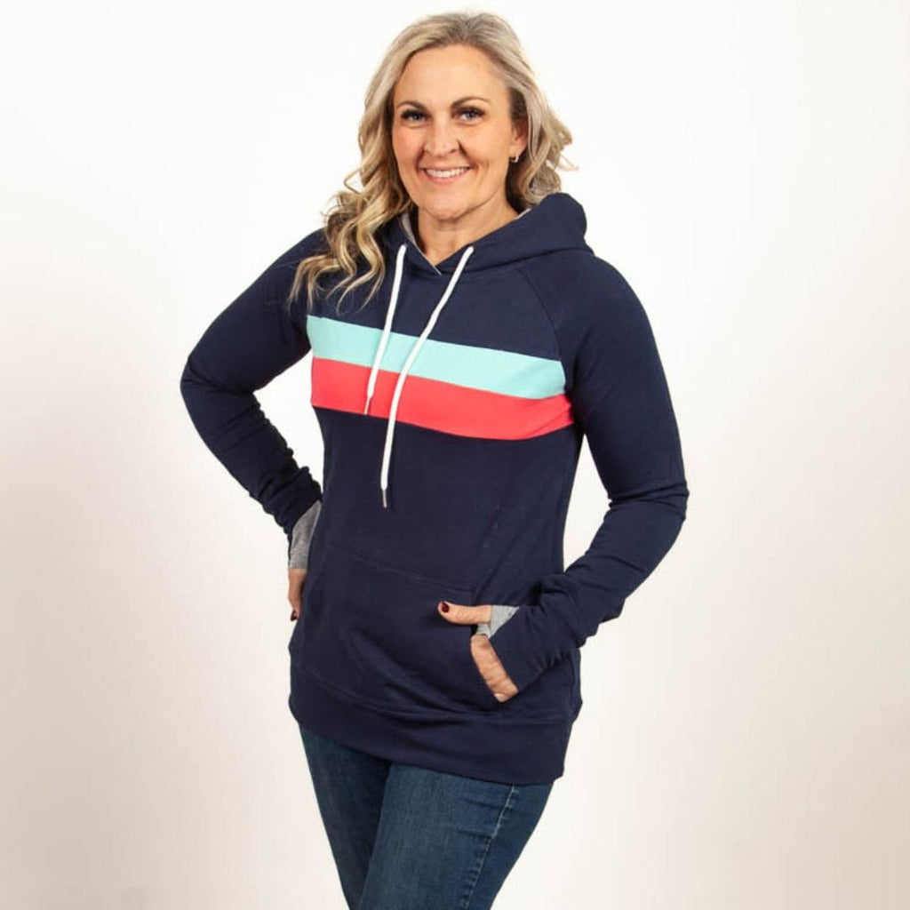 A woman wearing a navy pullover with coral and mint stripes, featuring thumbhole cuffs, kangaroo pocket, and a grey-lined hood. shown in size medium