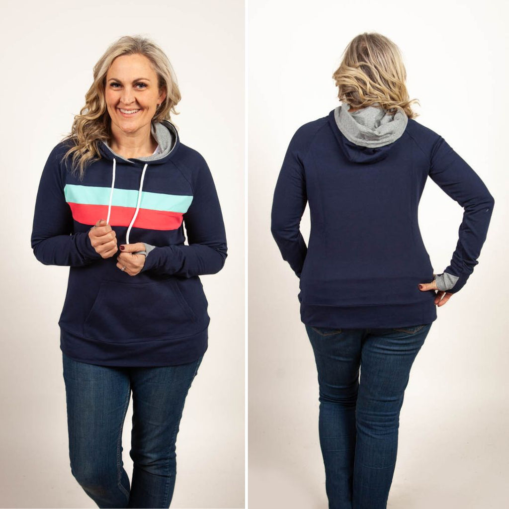 A woman wearing a navy pullover with coral and mint stripes, featuring thumbhole cuffs, kangaroo pocket, and a grey-lined hood. shown in size medium