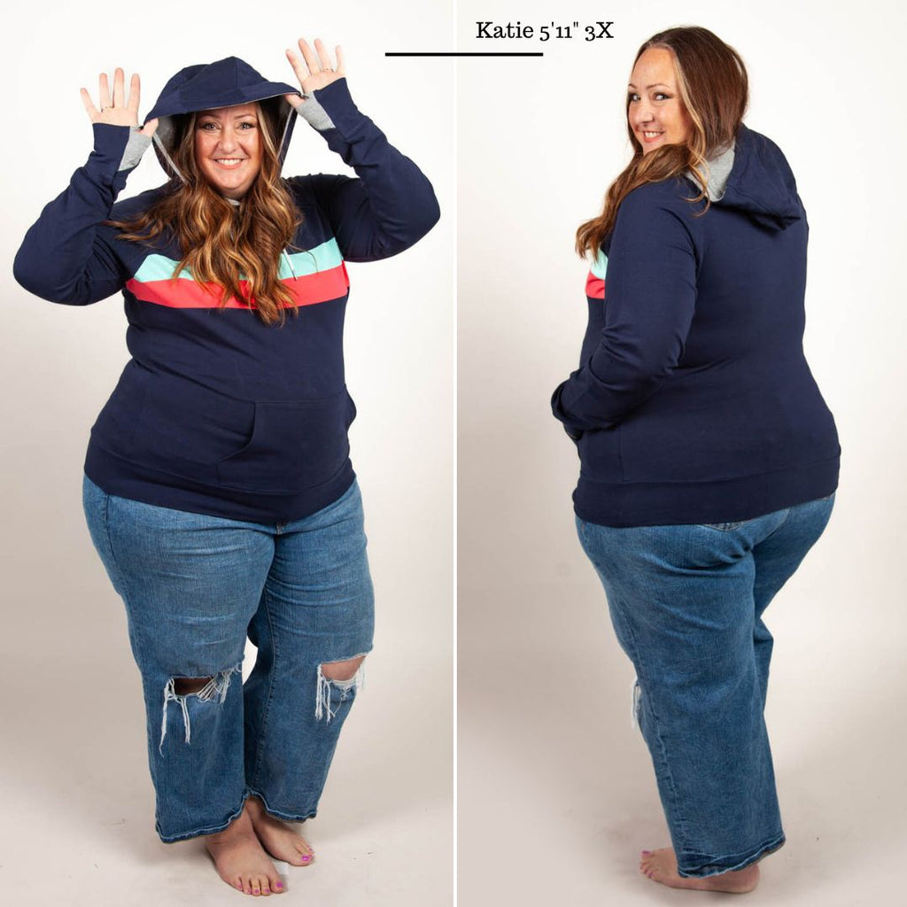 A woman wearing a navy pullover with coral and mint stripes, featuring thumbhole cuffs, kangaroo pocket, and a grey-lined hood. shown in size 3XL
