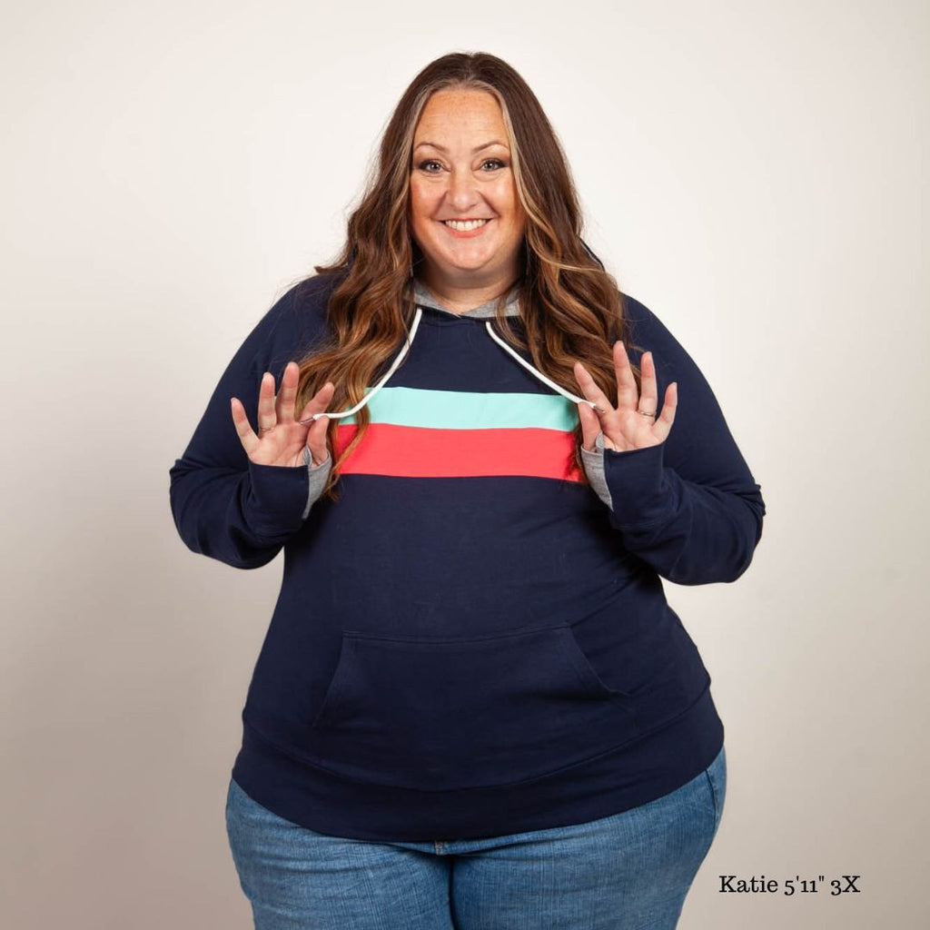 A woman wearing a navy pullover with coral and mint stripes, featuring thumbhole cuffs, kangaroo pocket, and a grey-lined hood. shown in size 3XL