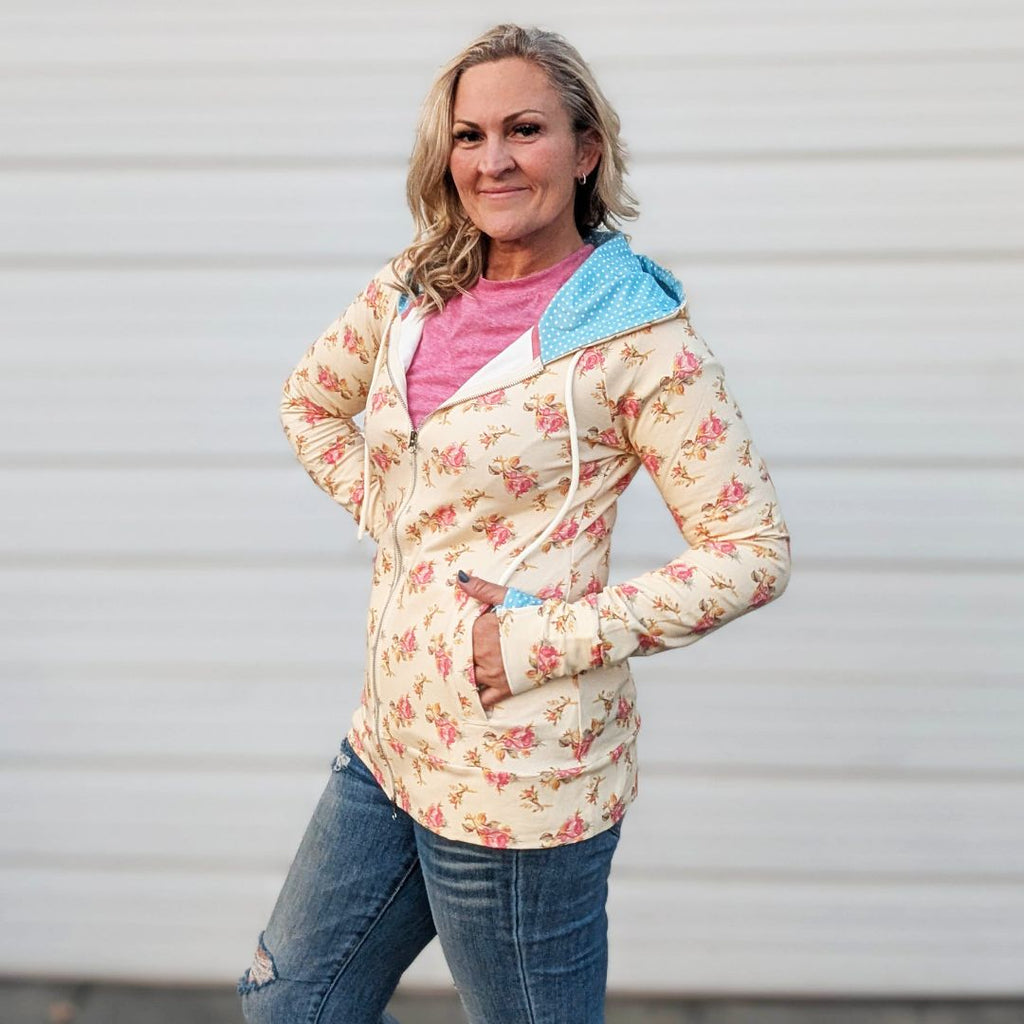 Woman wearing a full double zipper hoodie that has pink floral with cream background and blue with white polka dot accents in hood and thumbholes. shown in size medium