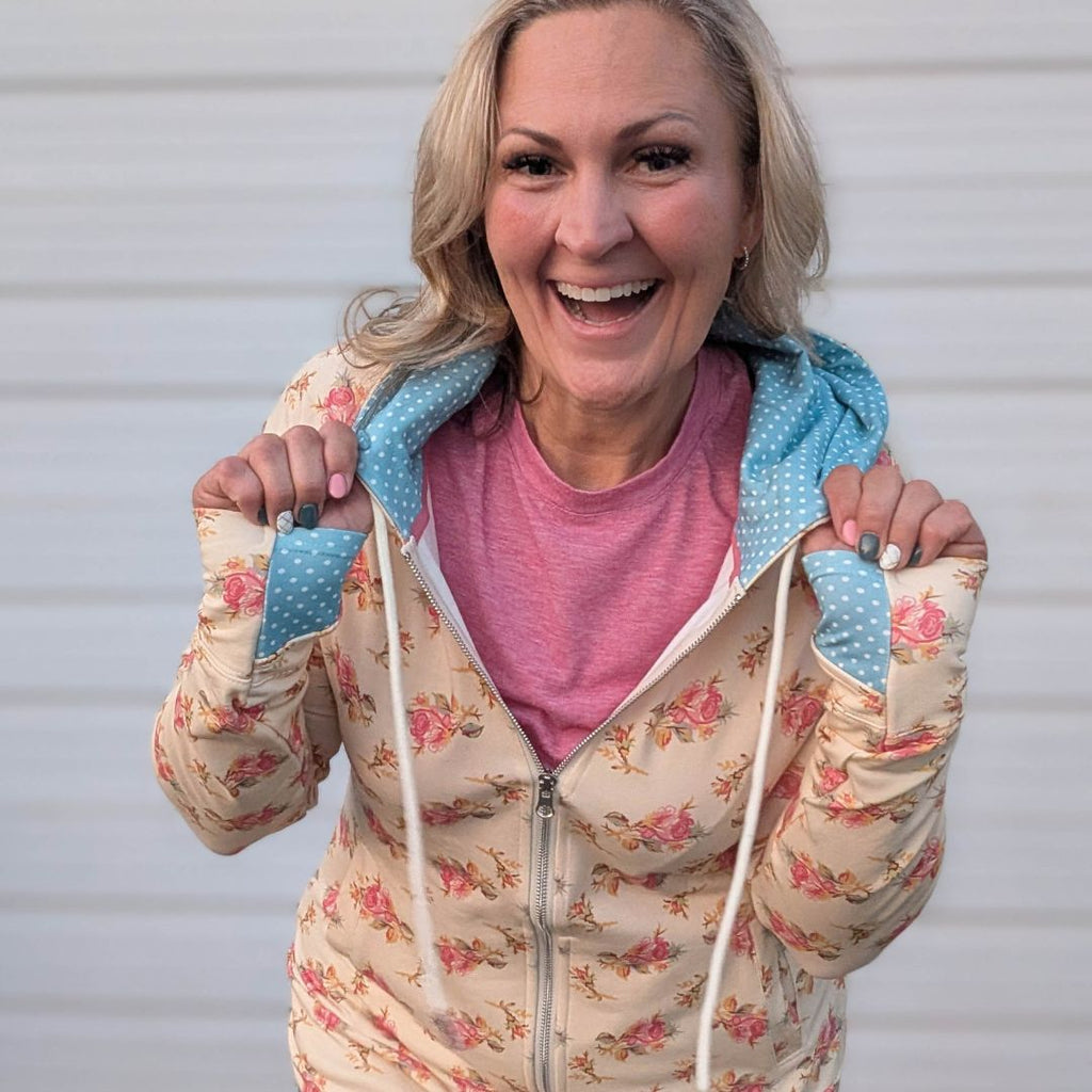 Woman wearing a full double zipper hoodie that has pink floral with cream background and blue with white polka dot accents in hood and thumbholes. shown in size medium