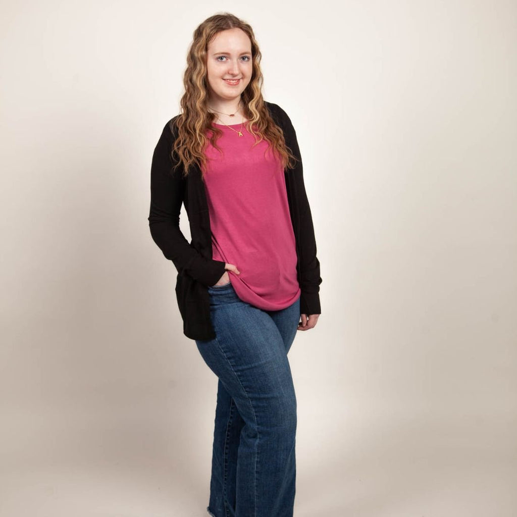 A woman wearing a pink crew neck shirt with short sleeves. paired with black essentials open cardigan. shown in size medium