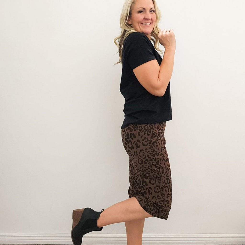 A woman wearing a knee-length pencil skirt with a leopard animal print, paired with a black studio crew shirt. shown in size medium