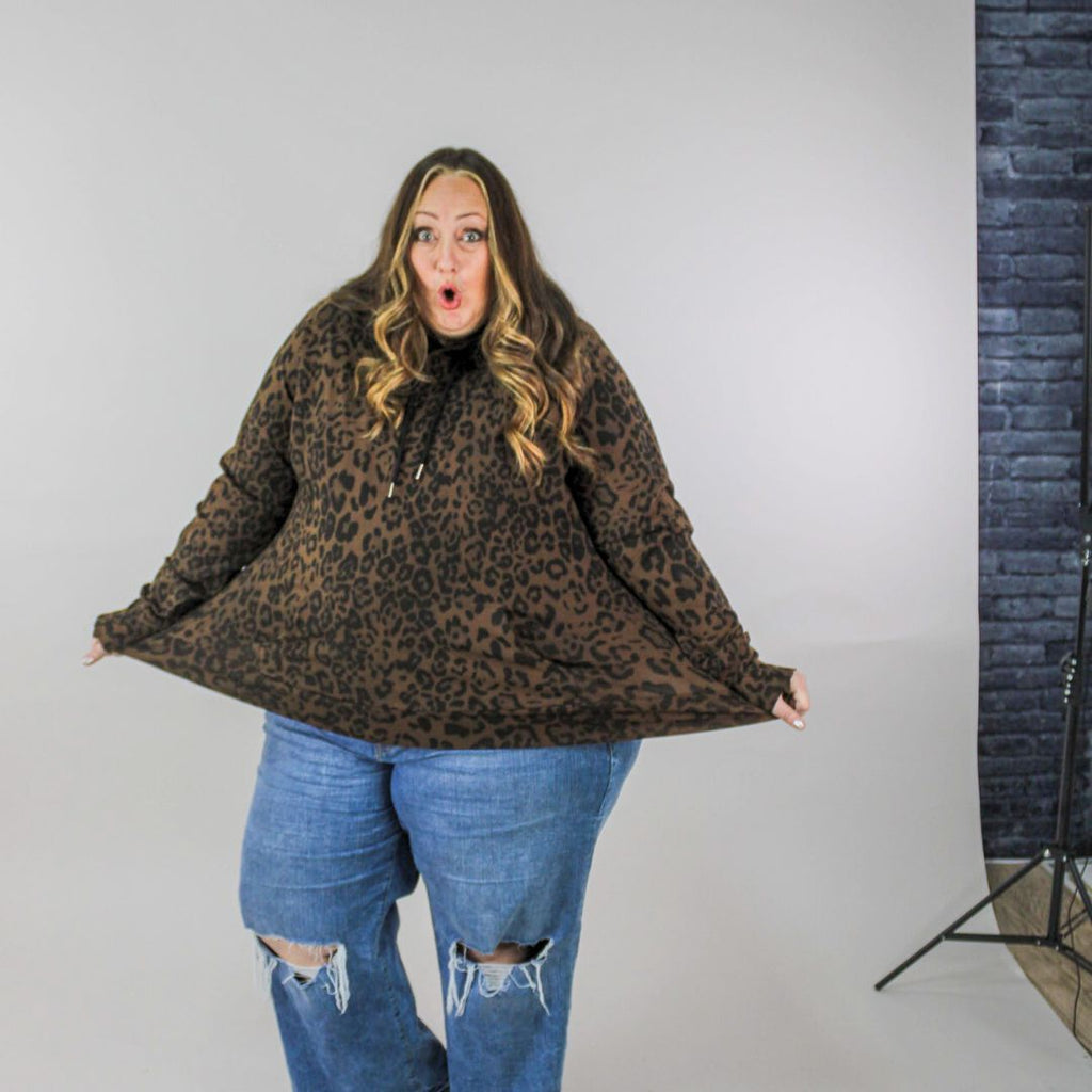 A woman wearing a brown leopard print pullover hoodie with a hood, thumbholes, and a kangaroo pocket. shown in size 3XL