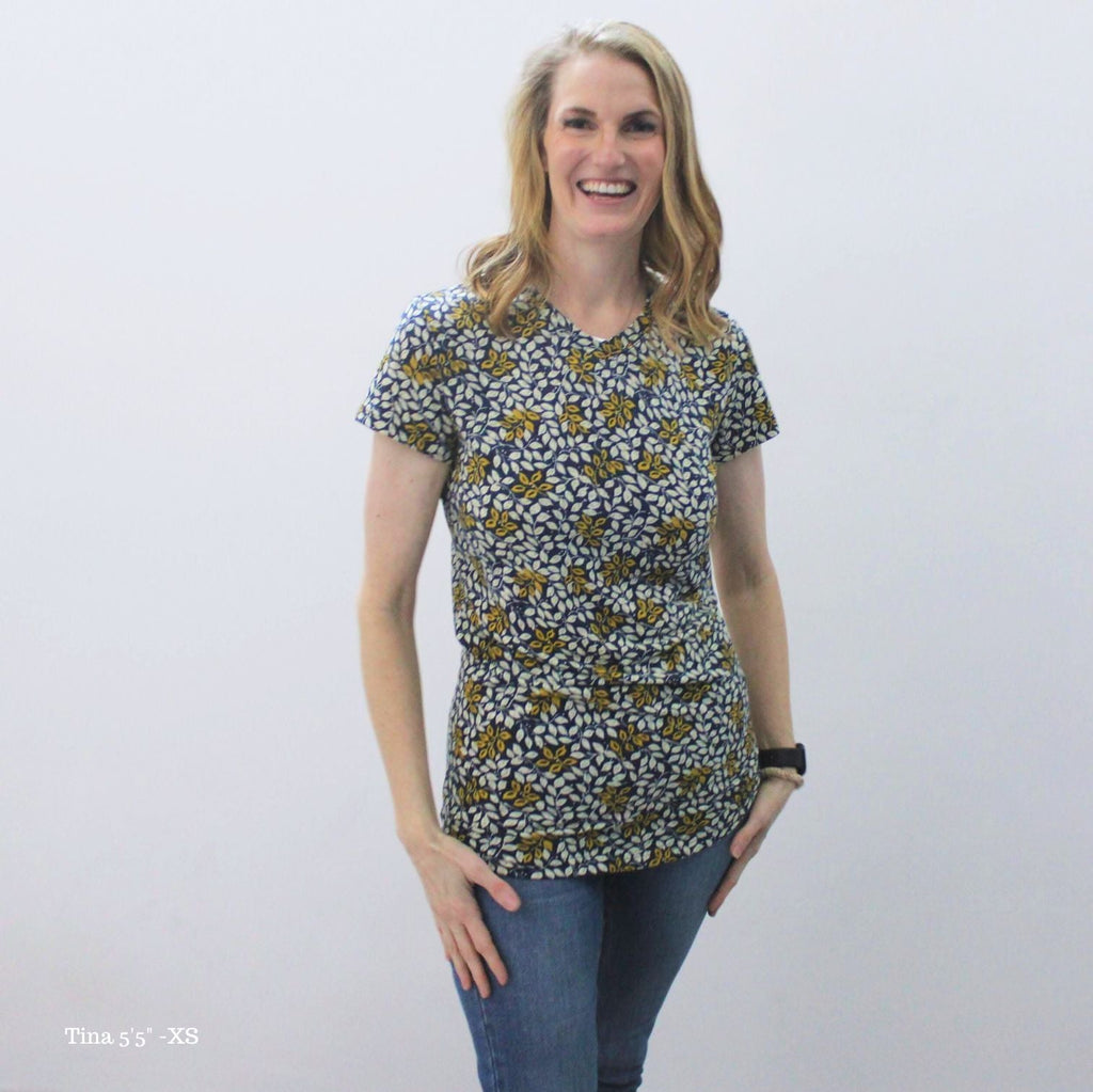 A woman wearing a v-neck shirt with a floral pattern in yellow and white on a dark blue background. shown in XS
