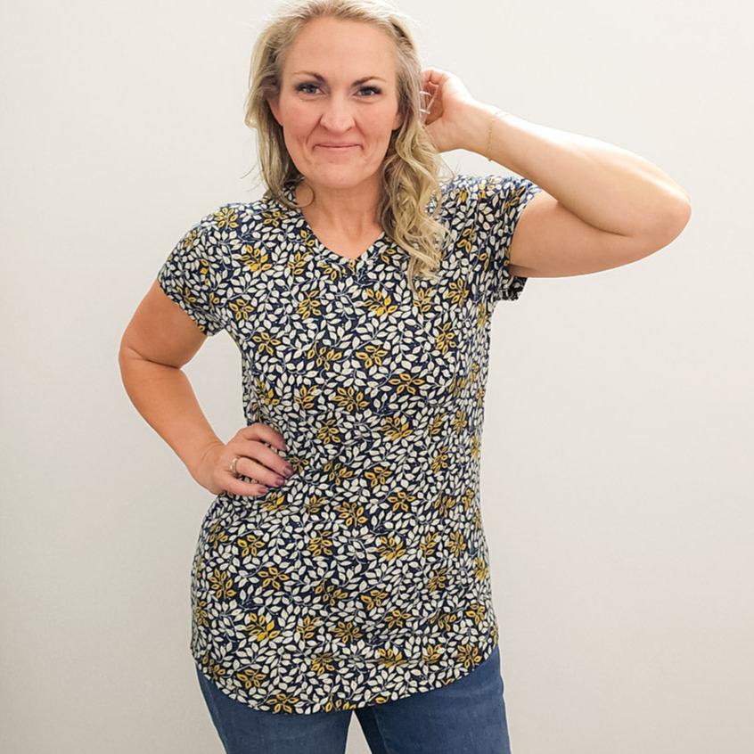 A woman wearing a v-neck shirt with a floral pattern in yellow and white on a dark blue background. shown in medium