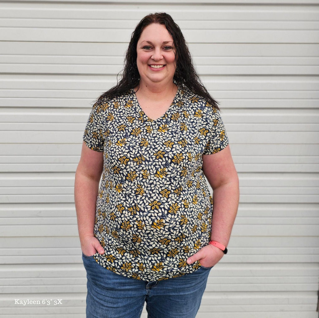 A woman wearing a v-neck shirt with a floral pattern in yellow and white on a dark blue background. shown in 3XL