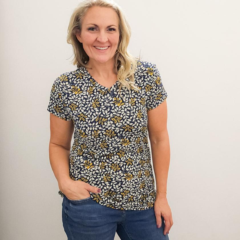 A woman wearing a v-neck shirt with a floral pattern in yellow and white on a dark blue background. shown in medium