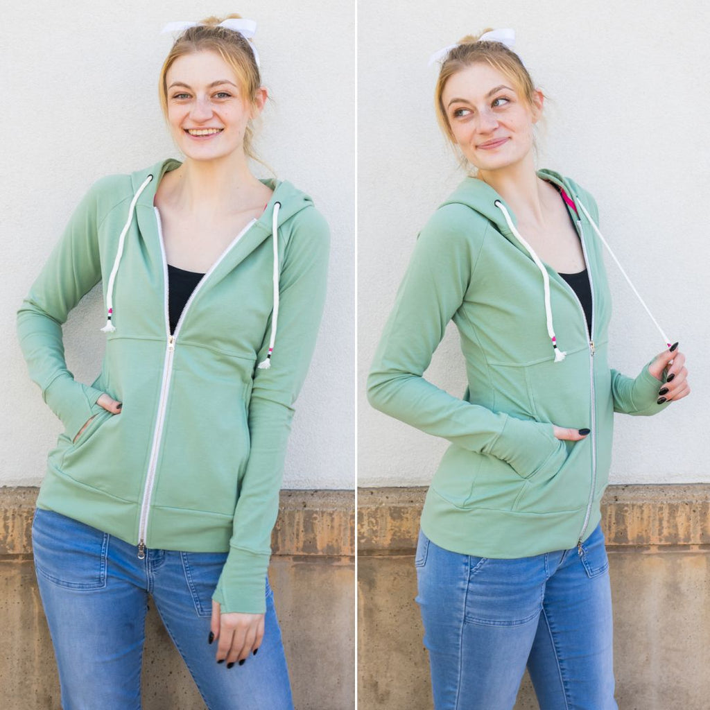 A woman wearing a green hoodie with a double zipper, pockets, and thumbholes. shown in size small